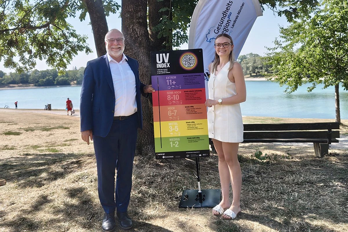 Martin Felber, Direktor der AOK München, und Kristina Rose, Leitung der im Landratsamt angesiedelten Geschäftsstellen der Gesundheitsregion plus, präsentieren die UV-Indextafel am Heimstettener See. (Foto: Landkreis München)